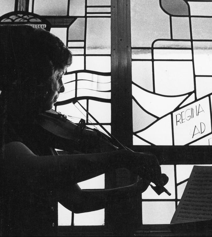 Student playing violin in front of stained glass